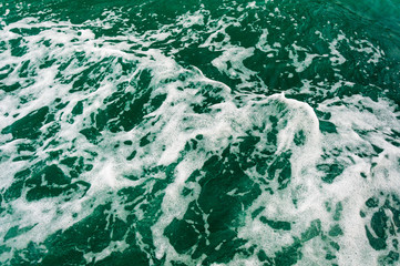 Dark turquoise sea water with white foam texture on the surface. Background image.