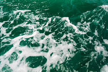 Dark turquoise sea water with white foam texture on the surface. Background image.