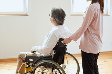 車椅子のシニアの男性を介助する若い女性