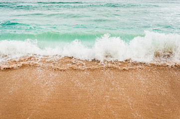The beach with the waves coming across the sand. Predominant blue, green and yellow colors.
