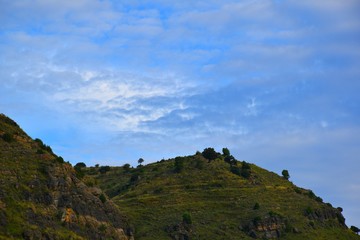 Rocky mountain, green grass and holm oaks with blue sky in different shades and clouds breaking.
