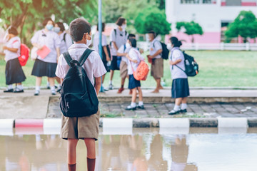 Male elementary school student wear face mask to prevent the Coronavirus(Covid-19) wait for her parents to pick her up to return home after school and the rain just stop in front of the school gate