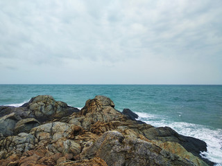 Fototapeta na wymiar brown rocks on the blue sea shore in cloudy day