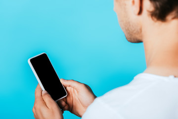 Cropped view of young man holding smartphone with blank screen isolated on blue