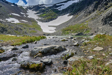 mountain river flowing from a lake formed by a glacier high in the mountains. Nice view of the mountain river and mountain slopes with snow