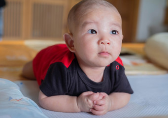 Curious Asian infant baby boy lie on the stomach or prone, wearing black red clothes on the bed