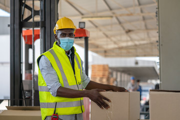 Man worker wear face mask in safety vest and yellow helmet preparing product input to box for...