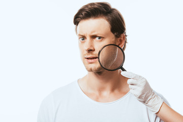 Dermatologist holding magnifying glass near pensive man isolated on white
