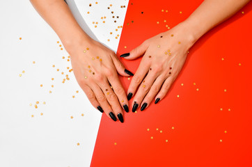 Stylish trendy female black manicure. Beautiful old woman's hands on white and red background with festive golden stars confetti