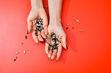 Stylish trendy female black manicure. Beautiful old woman's hands on red background with festive wooden confetti