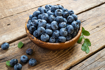 Fresh blueberry in wooden bowl. Juicy and fresh blueberries with green leaves on rustic table. Concept blueberry antioxidant for healthy eating and nutrition