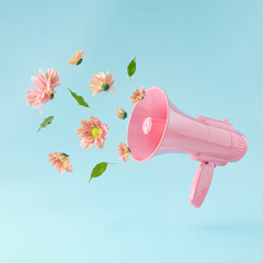 Pink megaphone with colorful summer flowers and green leaves against pastel blue background. Advertisement idea. Minimal nature concept.