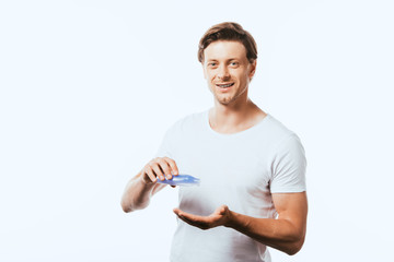 Young man looking at camera while pouring toner in hand isolated on white