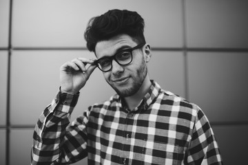 Portrait of young teen student in trendy eyeglasses and plaid shirt posing outdoors on wall background, handsome teen hipster guy standing outdoors looking at camera through stylish spectacles