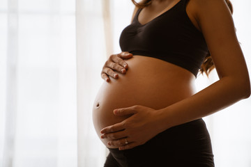 Close-up of a pregnant woman touching her belly on the foreground in emotional smile happy by asian woman