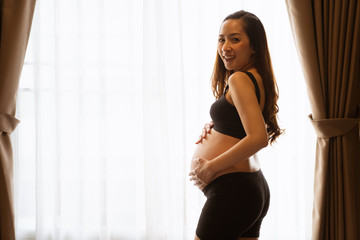 portrait of a pregnant woman touching her belly on the foreground in emotional smile happy by asian woman