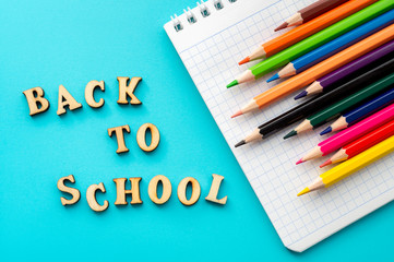 Wooden letters, notepad and color pencils on turquoise background. From above inscription Back to school and bright colorful pencils on turquoise surface. Concept of back to school and education.