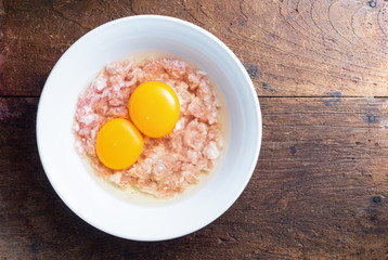 Minced pork with two of eggs in a white ceramic bowl on old wooden table, Prepare to cook the minced pork omelette menu
