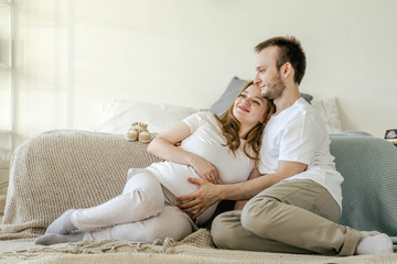 Family waiting for the baby. Husband and pregnant wife in a bright interior hug and smile. Pregnancy planning and preparation for childbirth