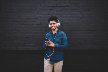 Happy hipster guy in headphones enjoying favourite music in modern headphones standing on copy space background, young stylish male student mobile enjoying audio book listening on smartphone
