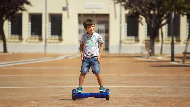 5-year-old boy skates safely and confident with a hoverboard in a town square during the day.