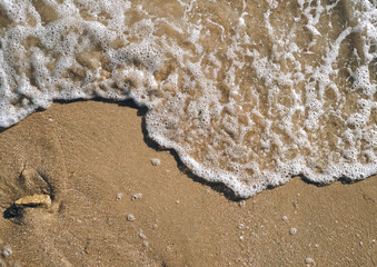 A sea wave with foam rolls over the sand, top view. Copy space.