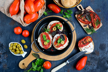 Juicy ripe tomatoes, sloth, olives and sandwiches with cheese and sun-dried tomatoes on a dark blue rustic table. Italian breakfast concept.