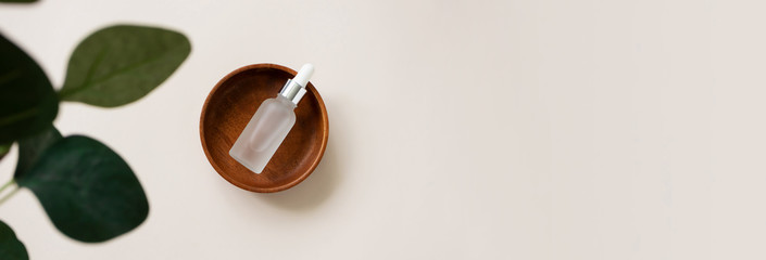 Vitamin serum in wooden plate and blur eucalypt leaf flat lay composition on light beige background...