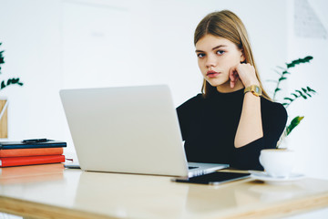 Portrait of beautiful student looking at camera while sitting at laptop device and in coworking space.Young woman with blonde hair using modern computer connecting to wireless 4G internet