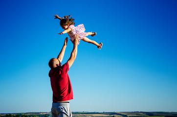 Happy father throws the baby up against the blue sky. A joyful child plays with his father. Happy family has fun in summer. Childhood. Conceptual photo freedom. Children's trust in their parents