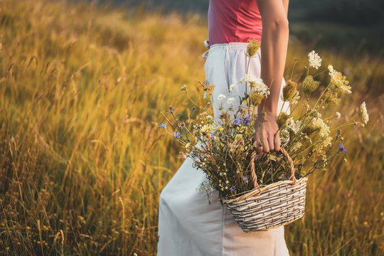 Woman walking with basket full of flowers  and enjoys in the nature.