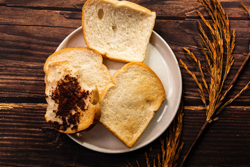 White bread smeared with chocolate Placed in a white plate On a dark old wood pattern background, top view concept