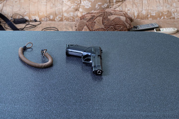 The gun is on the table. Pistol and sling on the home table. Storing a pistol at home.