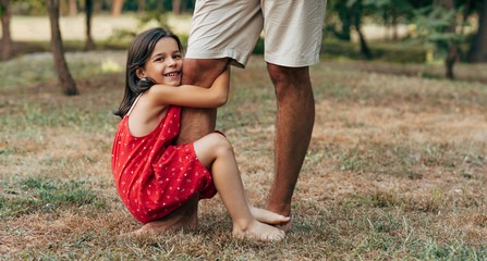 Cheerful smiling daughter spending time with his father swinging on daddy's leg outdoors. Ñute little girl playing with her dad in the park. Daddy and kid having fun together Happy father's day.