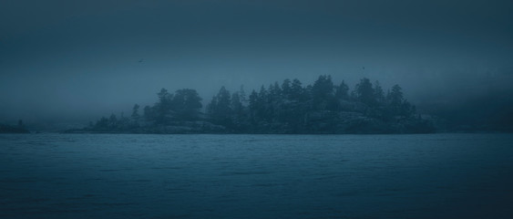 Silhouette of a forested island in the fog. Panoramic image.