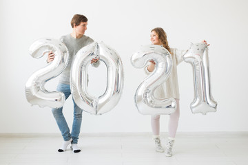 Holidays, festive and party concept - Happy loving couple holds silver 2021 balloons on white background. New Year celebration.