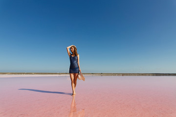 Fototapeta na wymiar Beautiful young girl with hat in hands on the salt pink lake at Genichesk, Ukraine. portrait a slim woman in short dress near the pink sea in summer day. travelling Ukraine