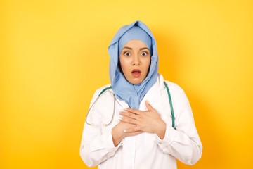 Scared Young arab doctor woman wearing medical uniform standing , looks with frightened expression, keeps hands on chest, being puzzled to notice something strange. People, hush reaction and emotions.