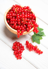 Fresh ripe red currant berries with leaves in a bowl on white wooden table. Healthy organic food, summer vitamins, BIO viands, natural background. Copy space for your advertising text message