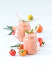 Vegetable smoothie of yellow, orange and red fresh tomatoes in a glass jar with a bamboo straw on a light background