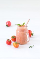 Vegetable smoothie of yellow, orange and red fresh tomatoes in a glass jar with a bamboo straw on a light background