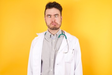 Portrait handsome Caucasian doctor man wearing medical uniform making grimace and crazy face, screaming out of control, funny lunatic expressing freedom and wild.