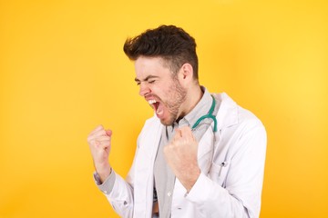 Young handsome caucasian doctor man wearing medical uniform, over isolated background very happy and excited doing winner gesture with arms raised, smiling and screaming for success. Celebration 