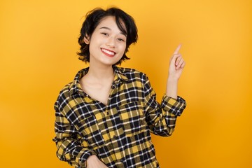 Photo of Young asian woman with short hair wearing plaid shirt standing over yellow background indicating finger empty space sales manager wear modern 