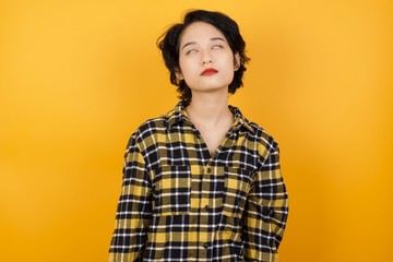 Young asian woman with short hair wearing plaid shirt standing over yellow background looking sleepy and tired, exhausted for fatigue and hangover, lazy eyes in the morning.