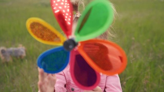 little daughter girl play pinwheel a wind toy. lifestyle happy family concept. child plays with windmill. girl blonde kid holds flower toy spinning pinwheel. happy childhood