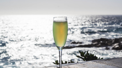 Una copa de cristal con pisco sour en una mesa de ébano con hermosas vistas al mar y un cielo despejado.Tonos suaves en un día templado,excelente para relajarse y darse un gusto.