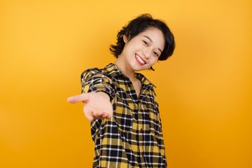 Young beautiful Asian woman wearing plaid shirt over yellow background smiling friendly offering handshake as greeting and welcoming. Successful business.