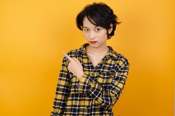 Young beautiful Asian woman wearing plaid shirt over yellow background. Pointing aside worried and nervous with forefinger, concern and surprise concept.