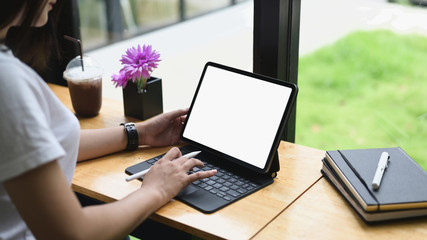Woman using mockup computer tablet with a white screen while sitting at the wooden counter bar.